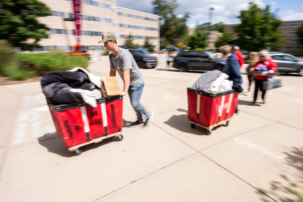 People push red move-in carts filled with belongings. 