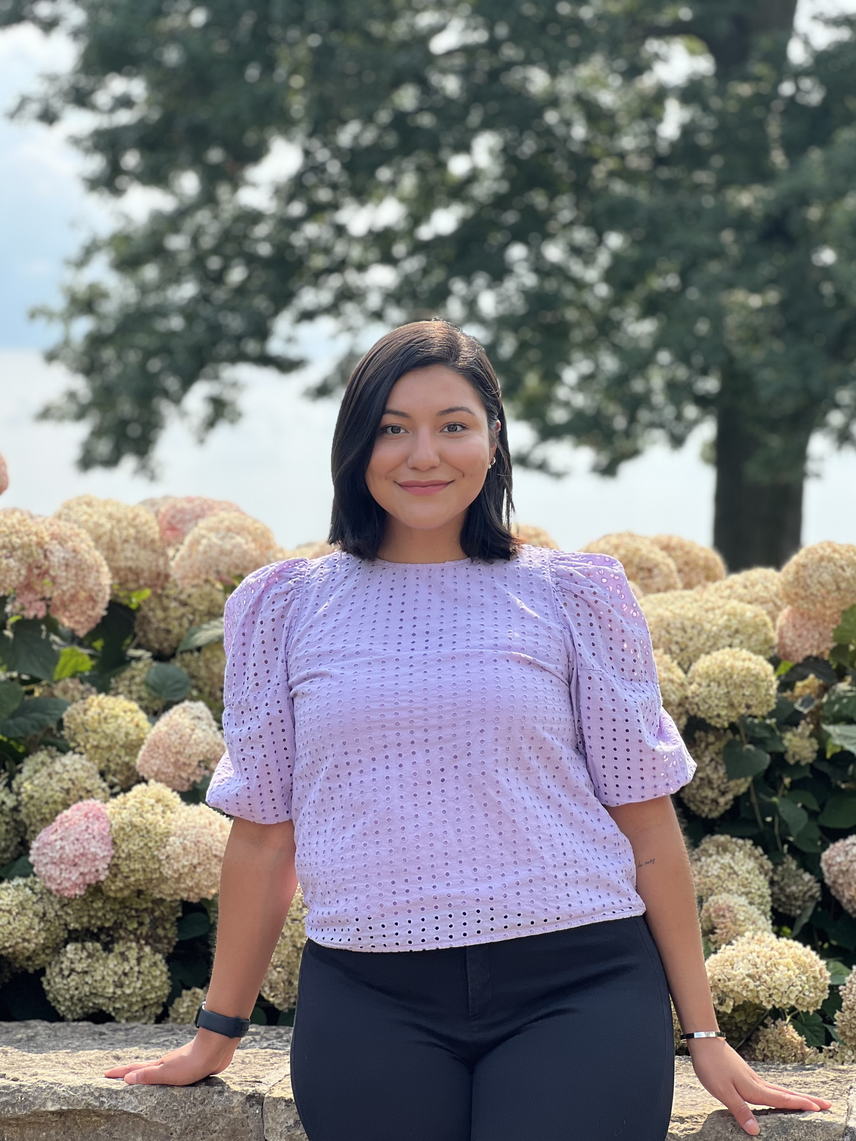Reyes stands for a portrait photo in front of a row of hydrangea flowers.