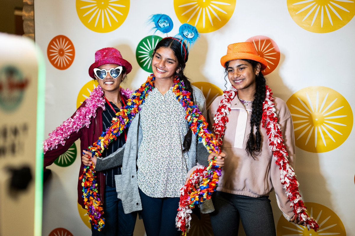 Three students pose in front of a branded banner. 