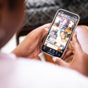 Tinnon sits on a chair and holds her phone. Over her shoulder, the screen shows an in-focus look at her social media page.