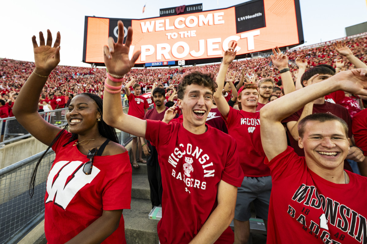 Students dressed in red stand in the stands of Camp Randall Stadium and cheer. 