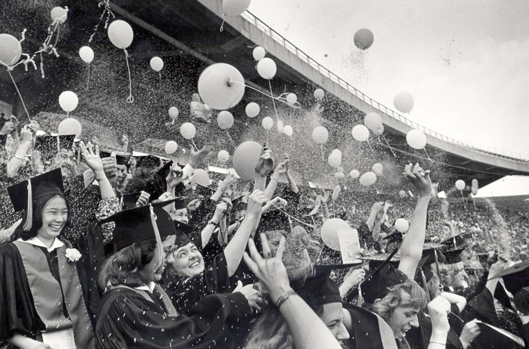 Grayscale image of graduates celebrating at Camp Randall with balloons and confetti in the air.