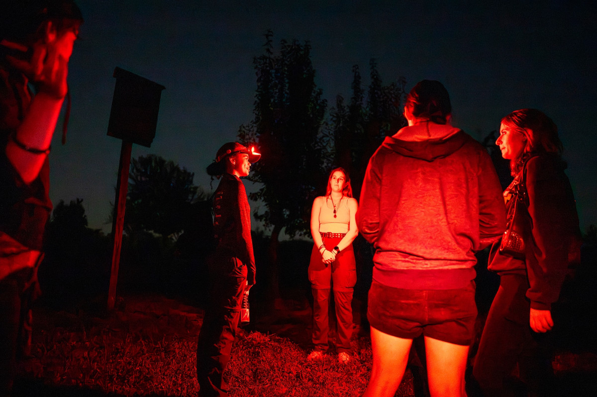 Students stand in a circle near a bat house wearing red light headlamps 