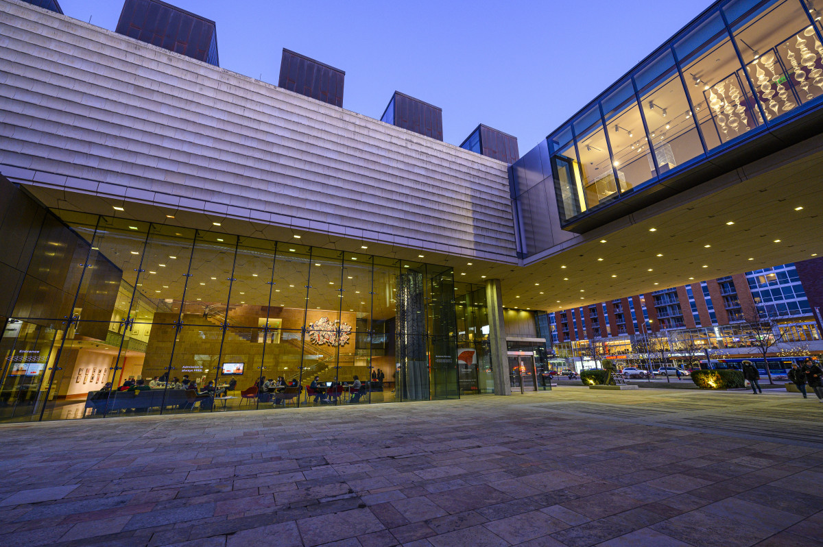A photo of the Chazen Museum of Art from the exterior, with the lights inside contrasting with approaching dusk outside.