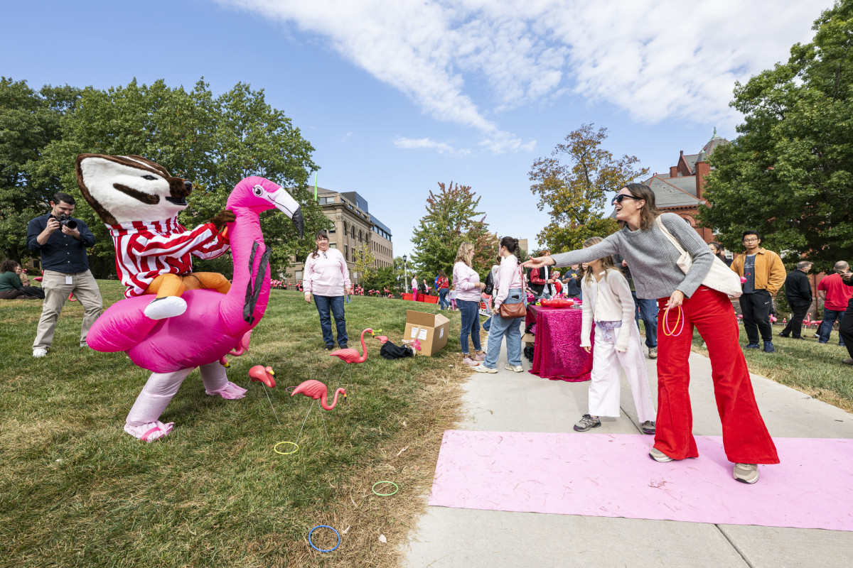 A family stands on Bascom Hill across from the Bucky Badger mascot. A woman tosses rings towards plastic flamingos planted in the ground.