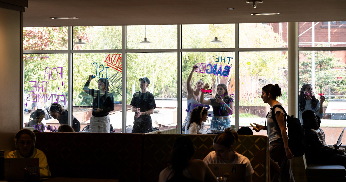 From inside Memorial Union, a group of students are shown drawing designs on the windows of the building's Lakeshore Lounge.