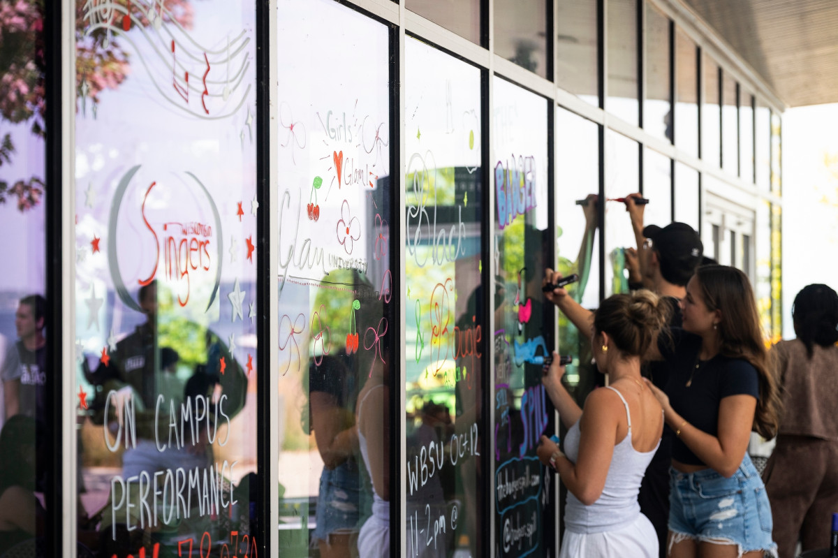A group of students, each holding large window markers, and designs on the windows of Memorial Union.