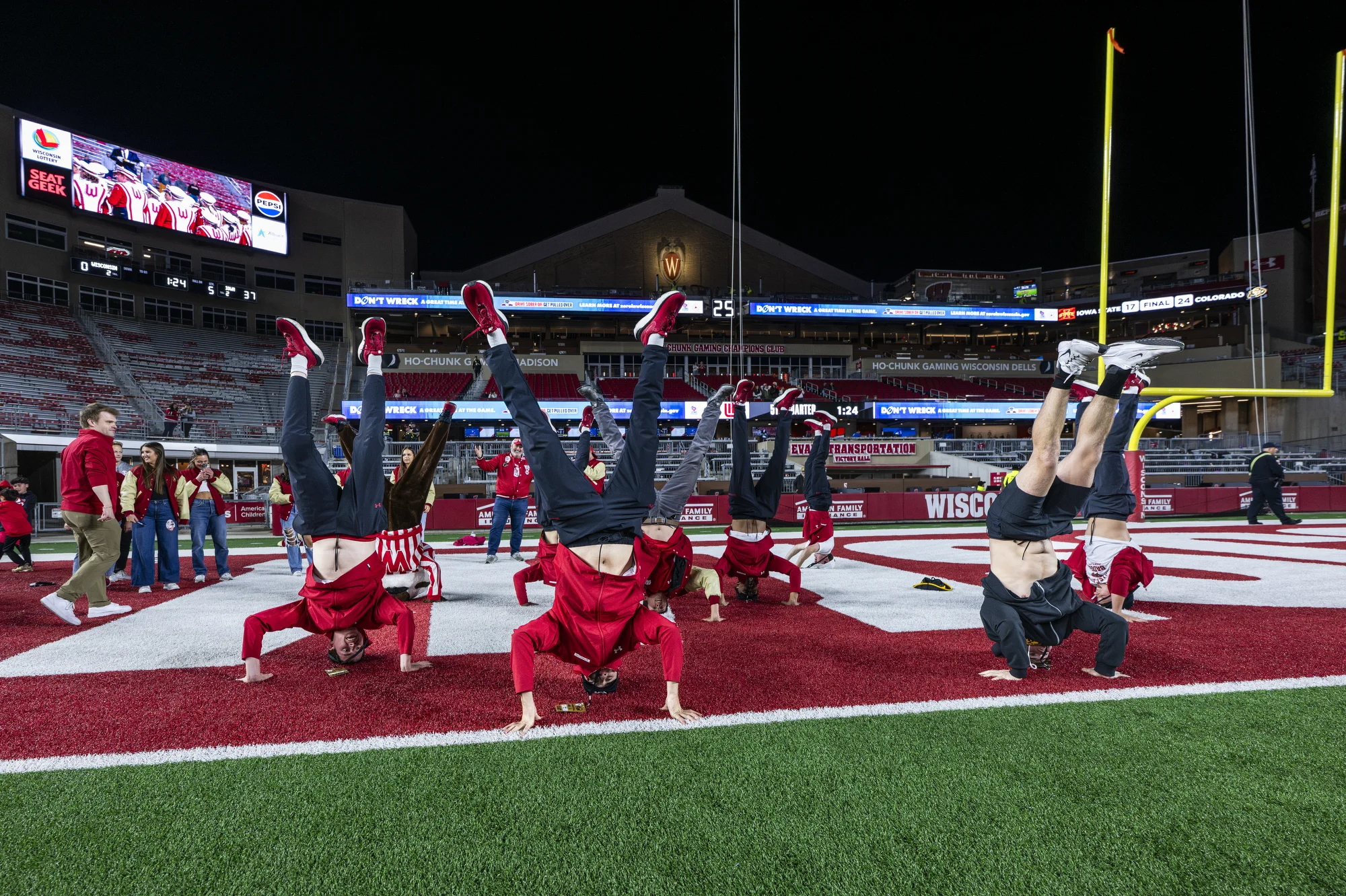 Several former Bucky Badger performers do hand stands together in the end zone of Camp Randall