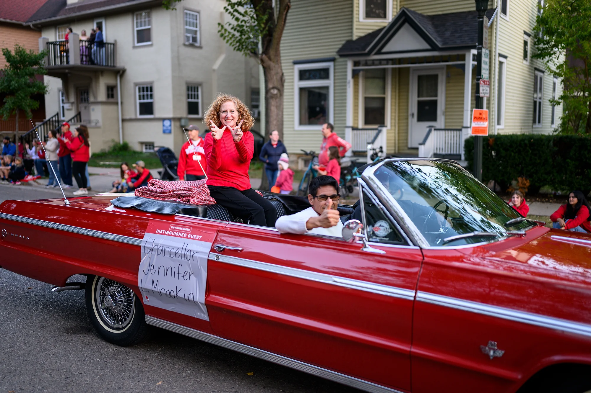 Chancellor Mnookin flashes the W sign with her hands while riding in a vintage red convertible during the Homecoming parade.