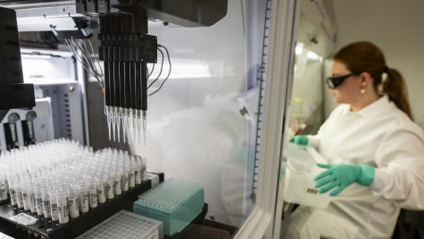 A Biomek i5 liquid handling machine processes samples of milk, with a researcher in medical protective equipment nearby.