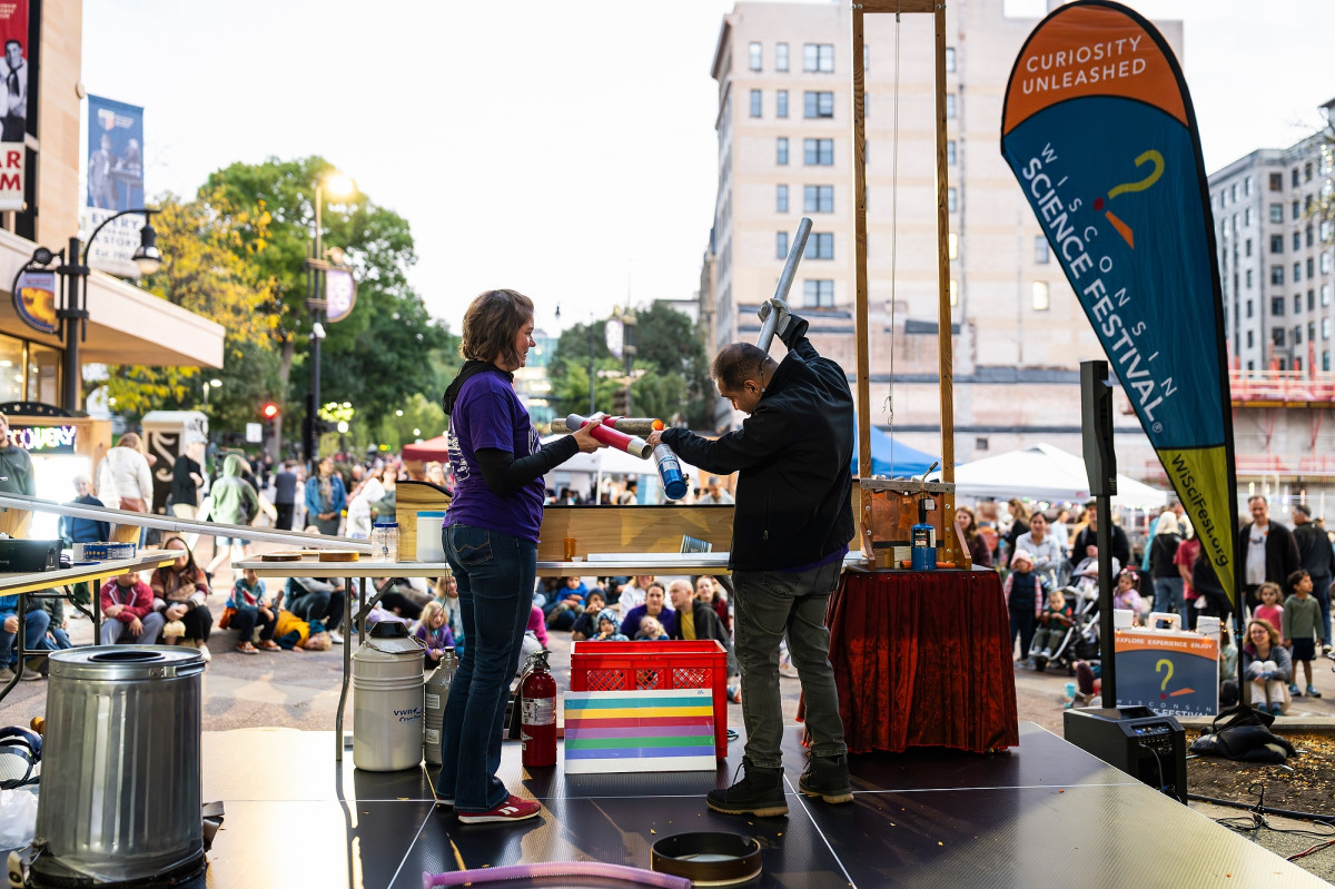 Two people stand on a stage in the middle of State Street preparing to wow the gathered audience with an explosive science demonstration.