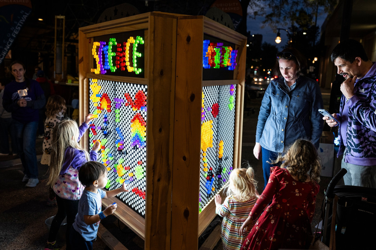 Parents and young children interact with a colorful light display board