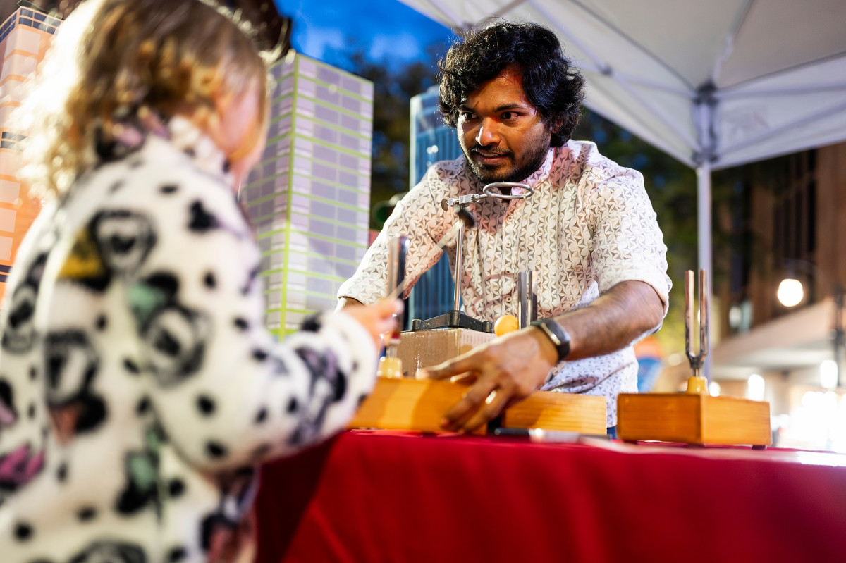 A graduate student at a demonstration booth interacts with a curious child.