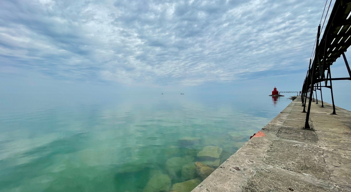Photo of a pier extending into teal blue water against a blue sky. the water and sky merge seamlessly at the horizon.