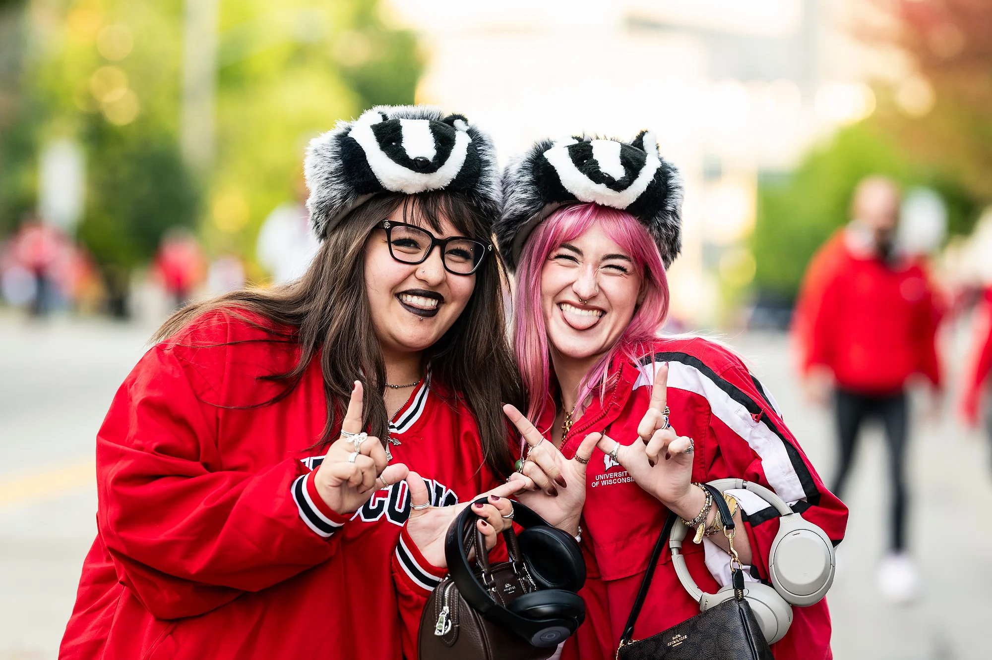 Two women wearing furry badger hats and red Wisconsin jerseys throw "w" signs and smile