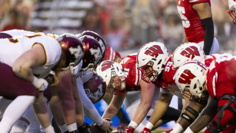 The Wisconsin Badgers defensive line stands opposite the Minnesota Gophers offense on a football field.