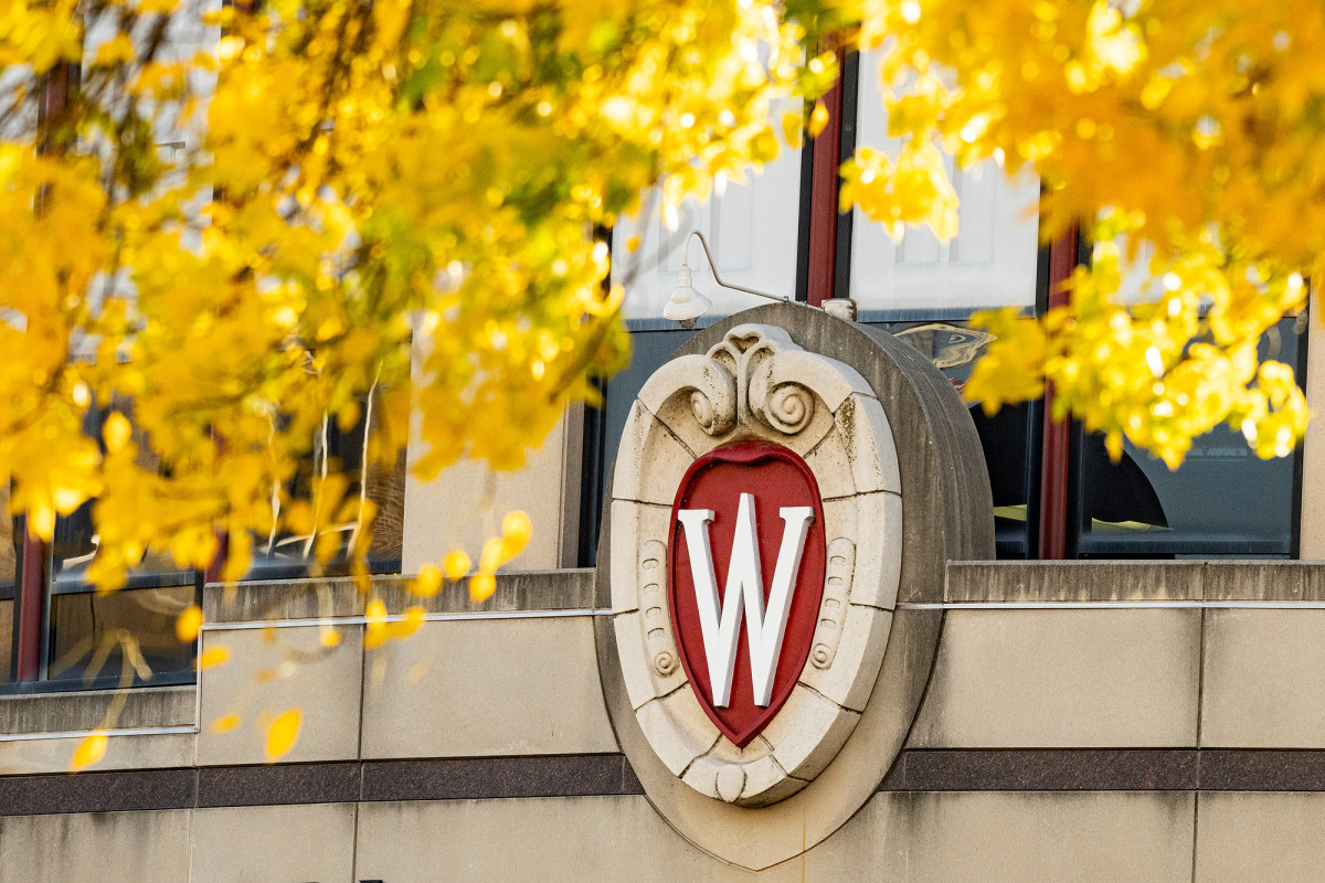 UW–Madison crest logo on the side of a building with yellow leaves framing it
