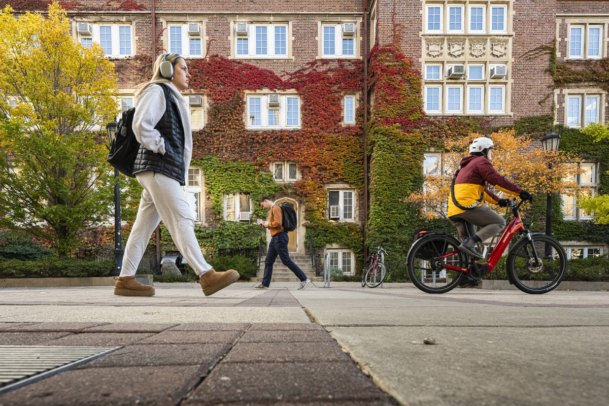 Pedestrians and a person on a bike traveling in front of a building covered in colorful plants