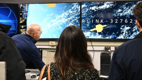 A group stands in front of large TV screens that display Starlink satellites.