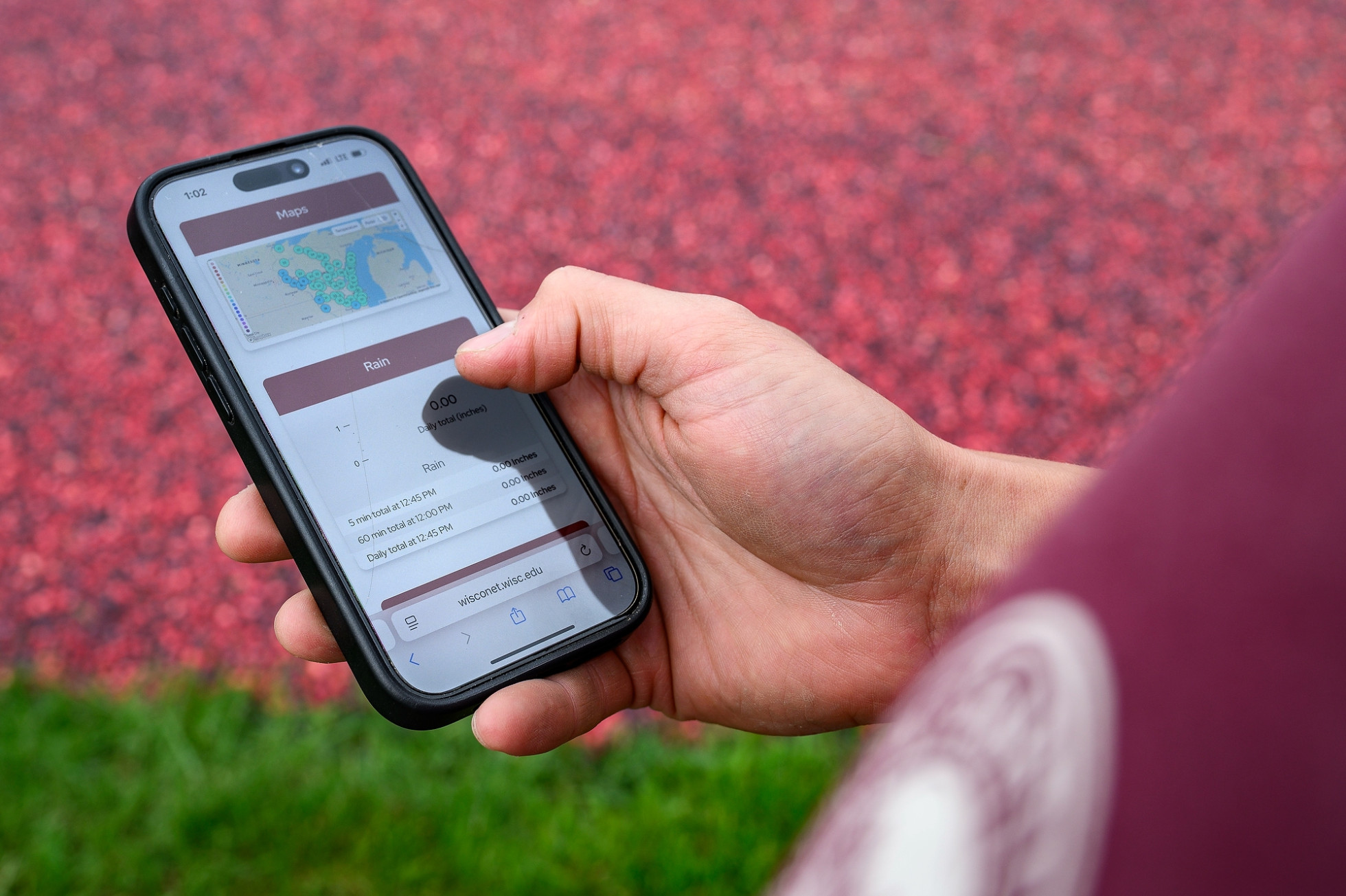 A close photo shows a hand holding a smart phone. Wisconet data is displayed on the screen.