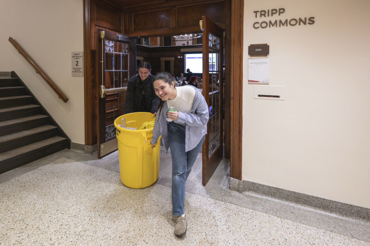 Two students haul a large garbage bin full of donated food out of the room.