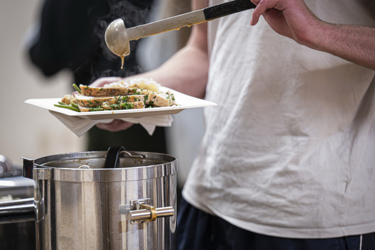 A close up of a student ladling gravy onto a plate full of turkey and mashed potatoes.