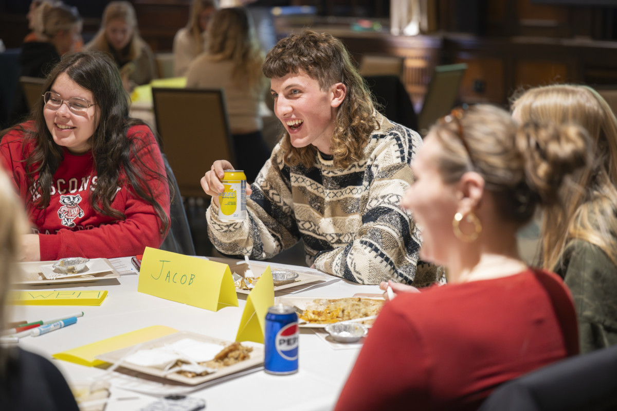 A student sits at a table with fellow Badger students and smiles at the discussion taking place.