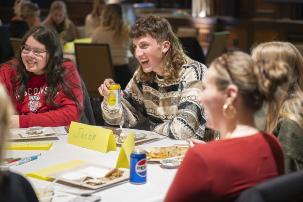 A student sits at a table with fellow Badger students and smiles at the discussion taking place.