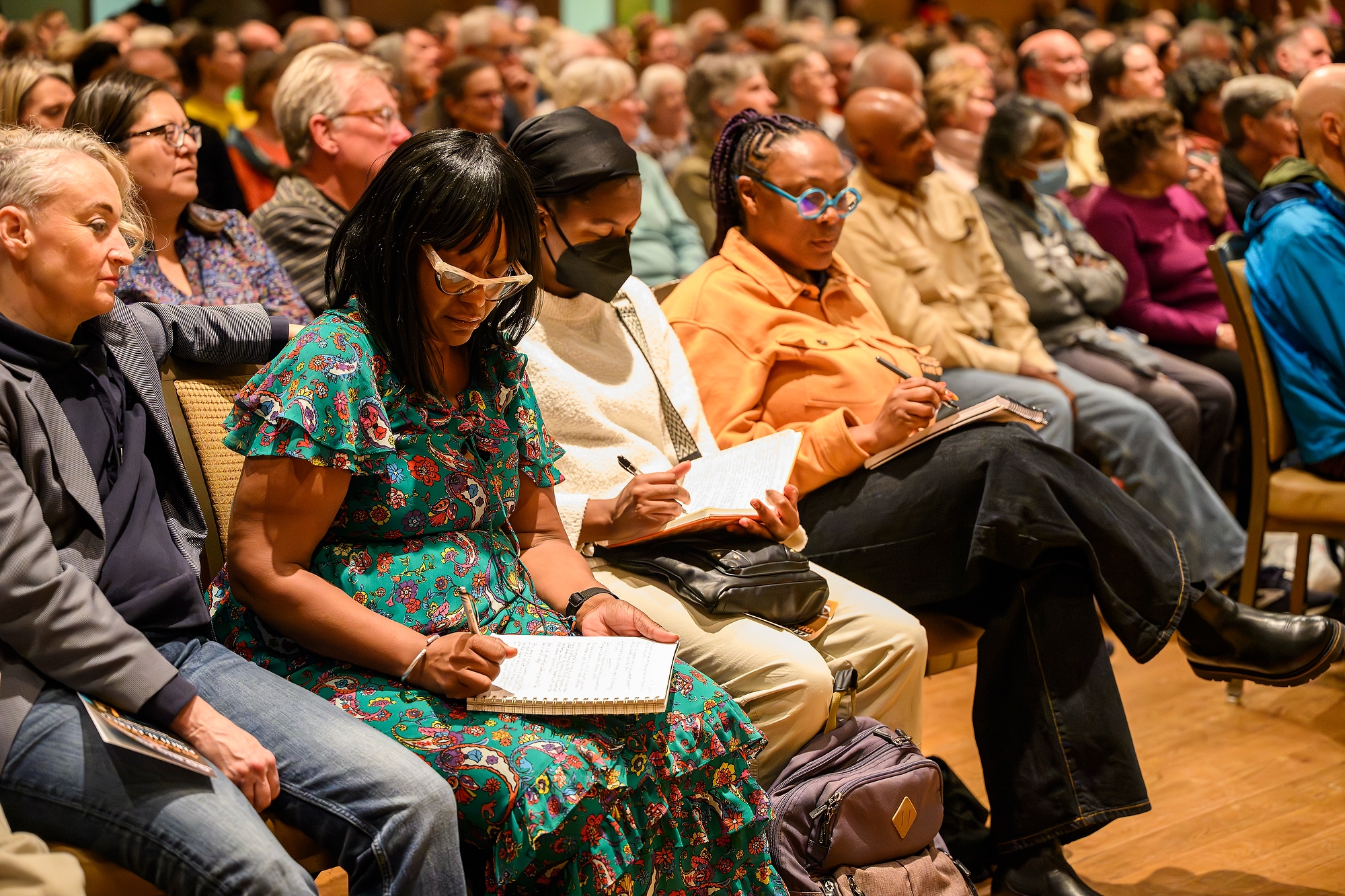 People sitting in an audience, some holding books, listen carefully.