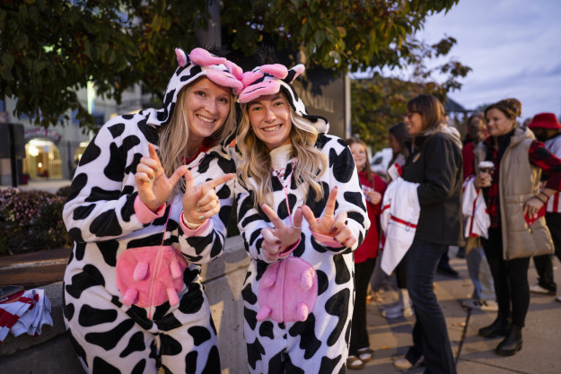 Two people dressed as cows hold up 'w' signs outside of the UW Field House.