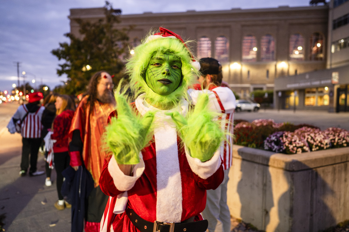 A student wearing a Grinch costume holds up a 'w' sign outside of the UW Field House.