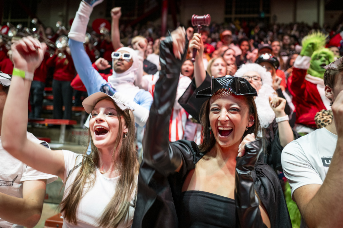A group of students all dressed in different costumes cheer on the women's volleyball team.