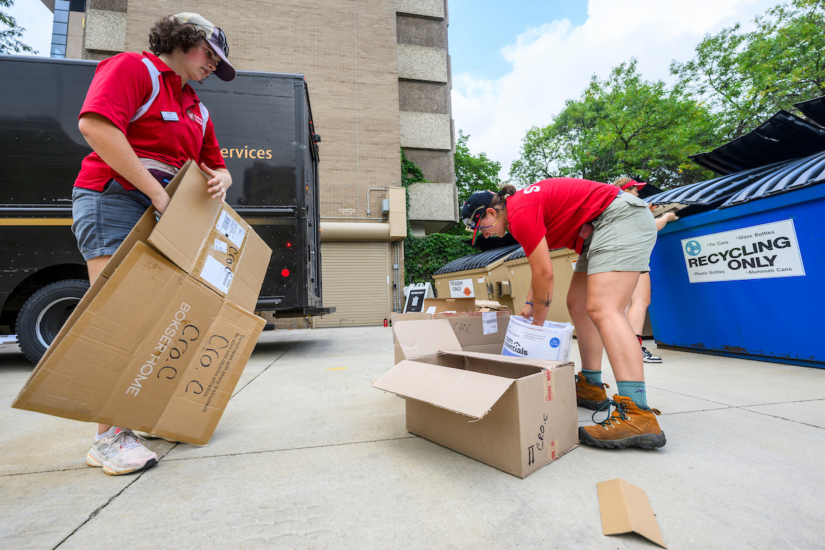 Students break down cardboard boxes in a parking lot.