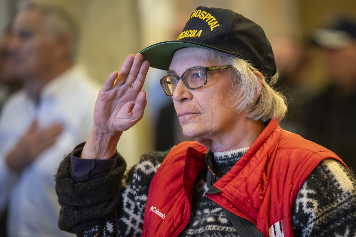 A woman wearing a U.S. Navy hat stands at attention with her hand in salut.