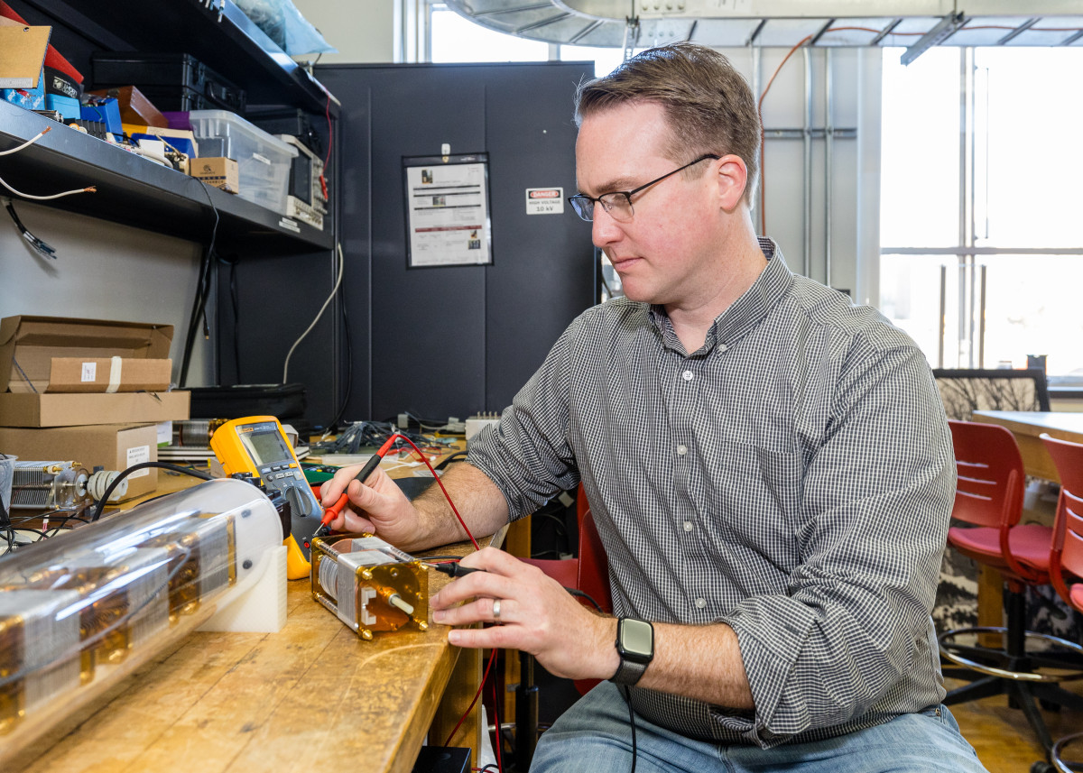 A man sits at a table and works on a small electrical motor.