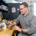 A man sits at a table and works on a small electrical motor.