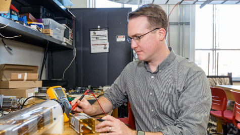 A man sits at a table and works on a small electrical motor.