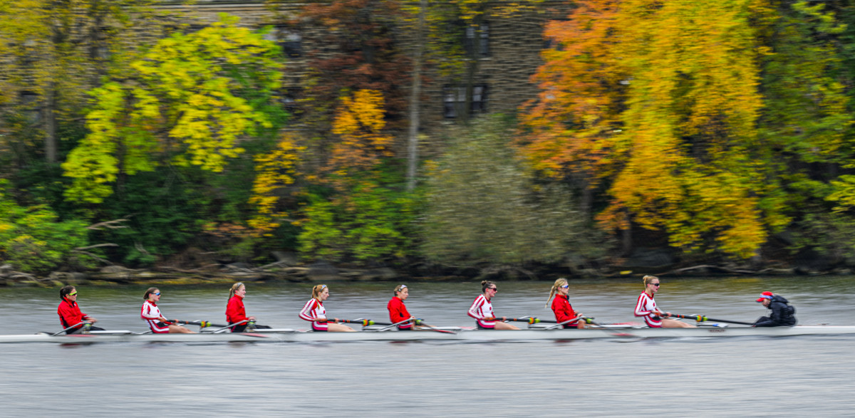 Crew team rowing on the water with fall leaves in the background