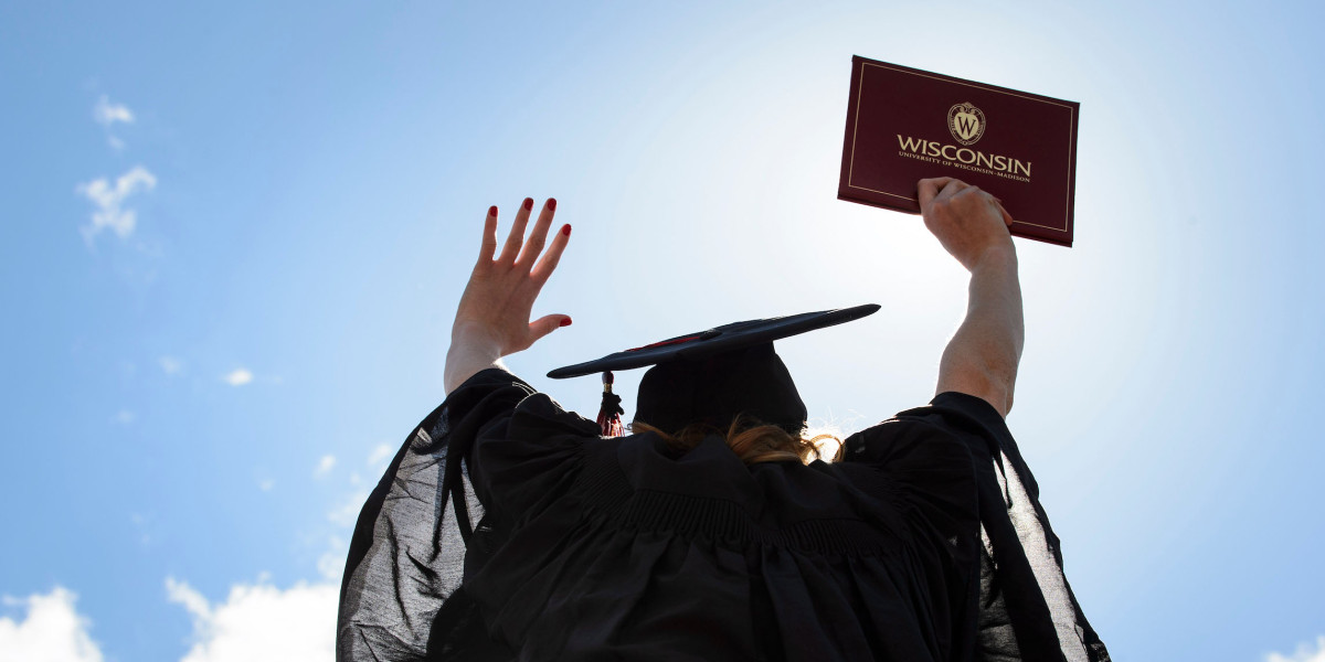 A student wears a graduation robe and cap and lifts her diploma up in the air.