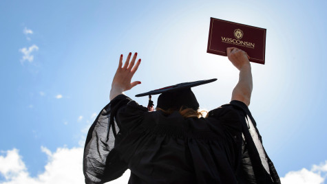 A student wears a graduation robe and cap and lifts her diploma up in the air.