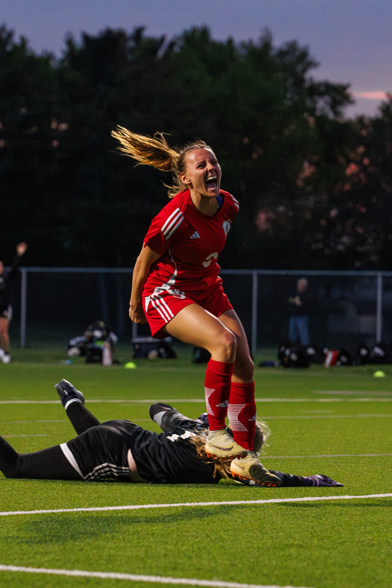 A young woman wearing a soccer uniform yells in celebration on a soccer pitch.