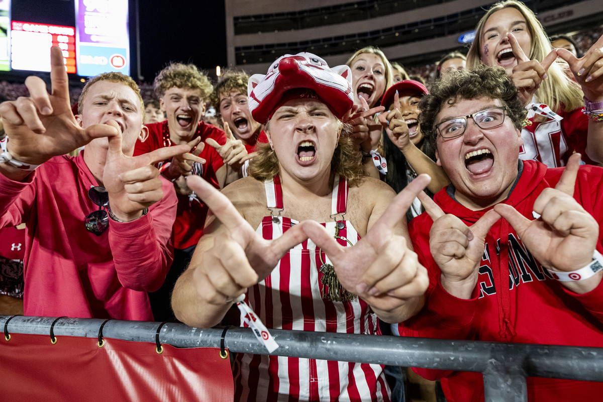 Excited students wearing Badger attire make the "W" with their hands while cheering