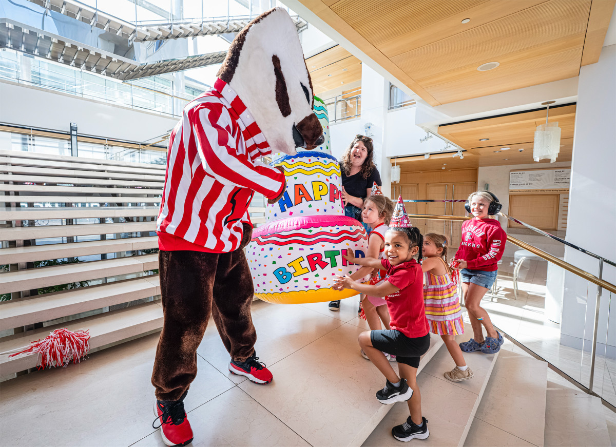 Bucky Badger mascot holds an inflatable birthday cake with a group of children