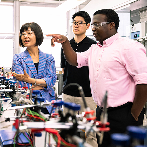 Three people looking at a monitor next to a bench of scientific equipment