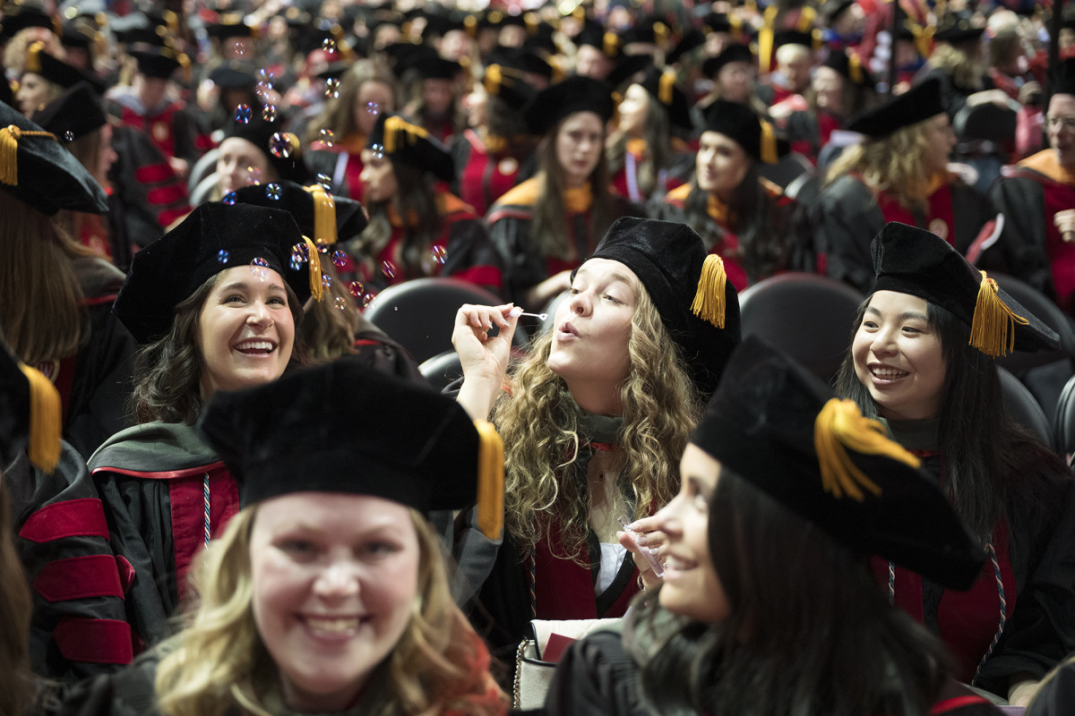 A graduate blowing bubbles surrounded by other smiling graduates