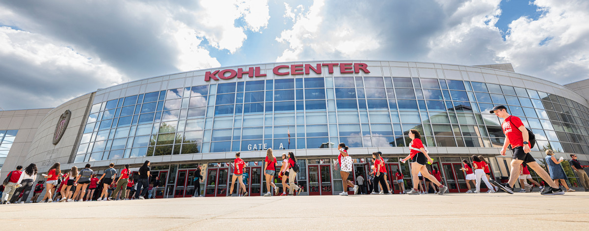 Groups of people walking in front of the Kohl Center on a sunny day