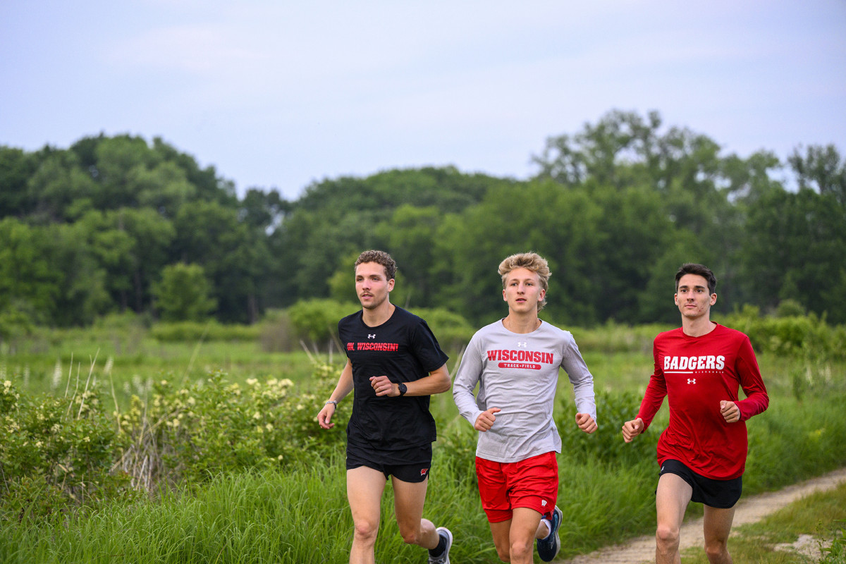 Three people in Wisconsin Badger attire jogging through a grassy area