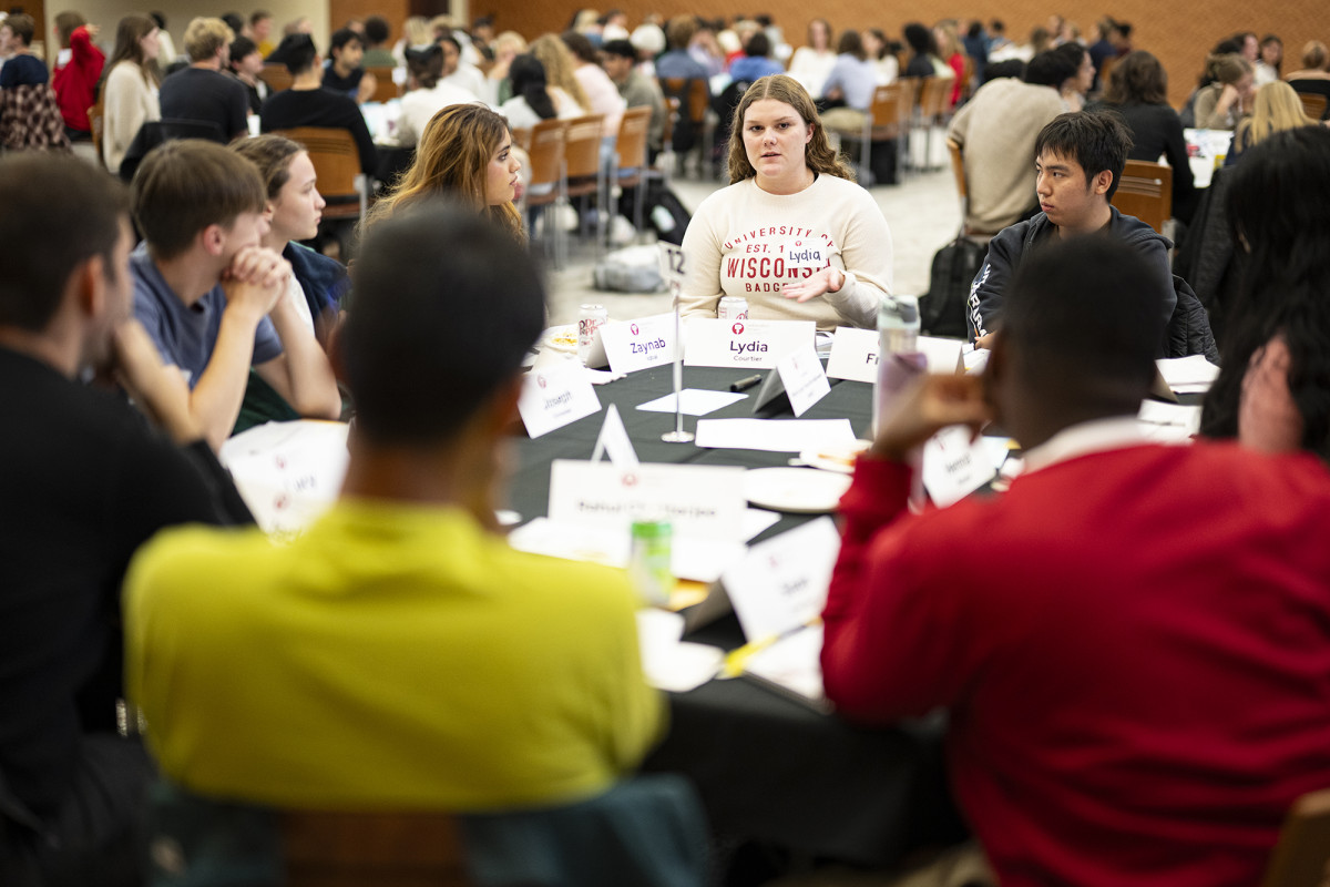A group of people conversing around a table in a large room filled with people