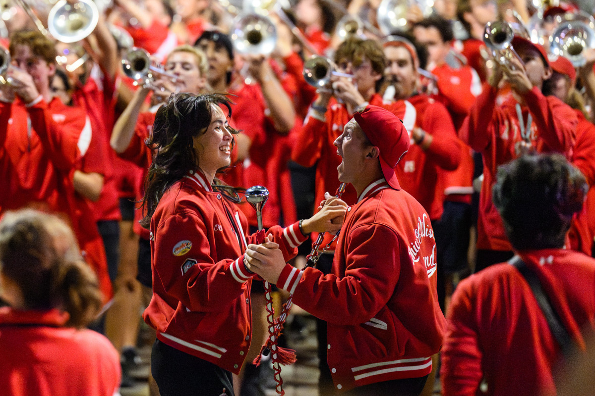 Two people smiling and dancing with each other while a marching band plays around them