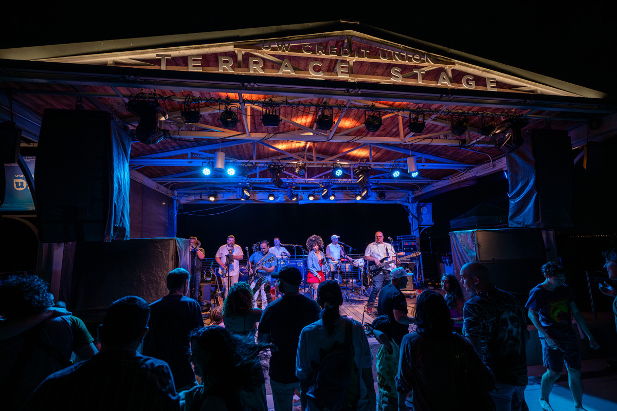 A band playing on an outdoor stage at night with an audience looking on